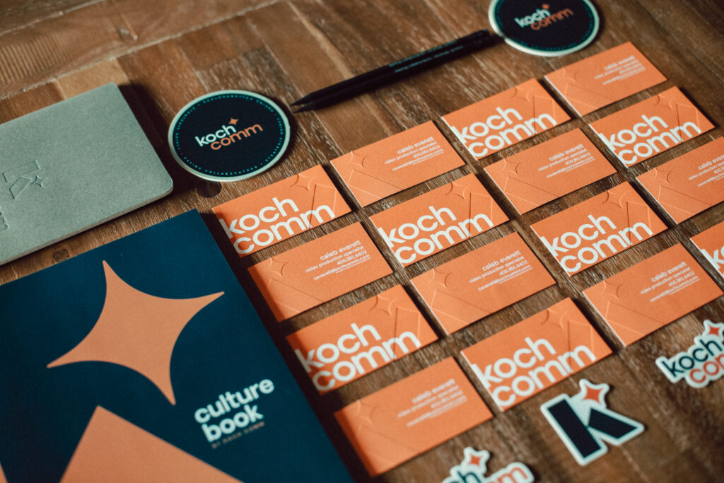 Koch Comm's rebranded collateral including a culture book, stickers and business cards.